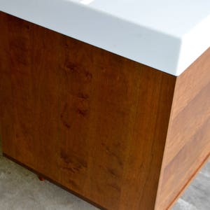 May include: A wooden cabinet with a white countertop. The cabinet has a light brown wood grain finish.