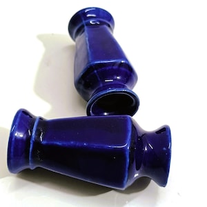 Puede incluir: Dos pequeños jarrones de cerámica de color azul cobalto brillante con forma hexagonal. Cada jarrón presenta un cuello estrecho que se ensancha en el borde superior y una base más ancha. El esmalte liso y reflectante muestra variaciones.