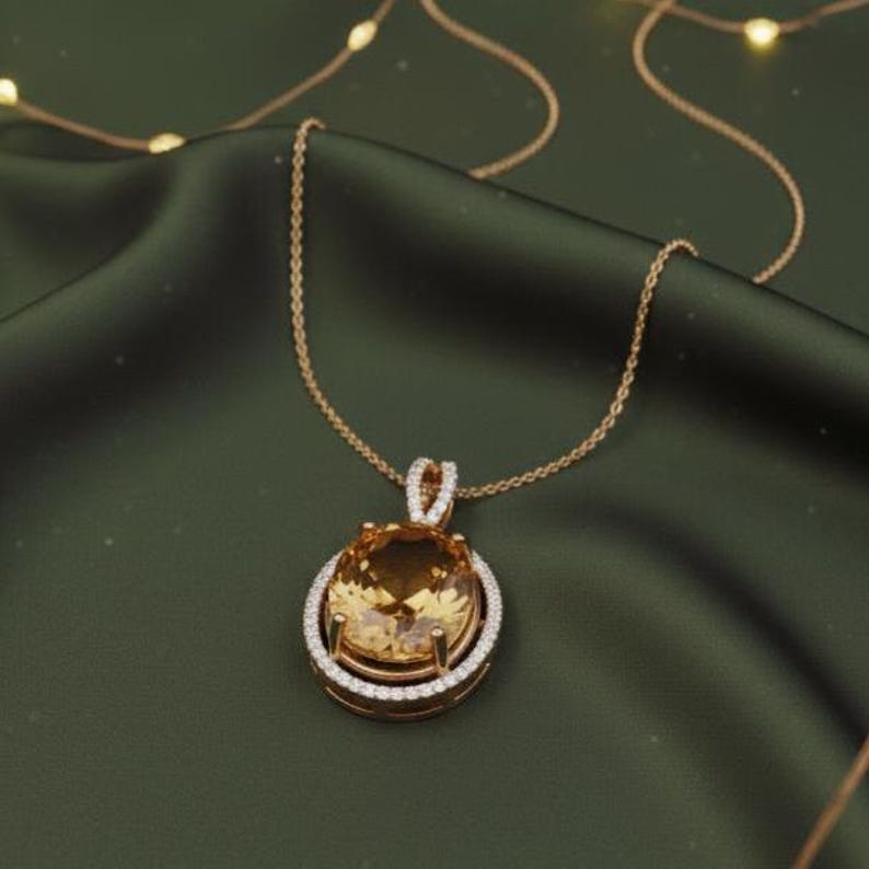 May include: A gold necklace featuring a large, oval, amber-coloured gemstone pendant. The pendant is surrounded by a halo of small, sparkling white stones. The necklace chain is delicate and gold, set against a dark green backdrop.
