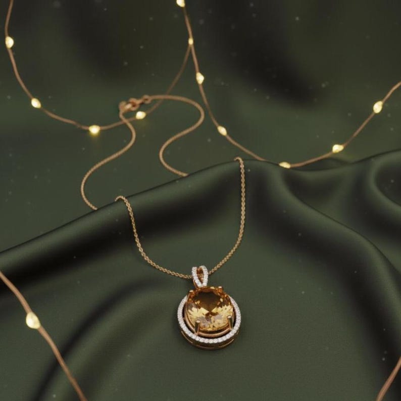 May include: A gold pendant necklace featuring a large, oval, amber gemstone, surrounded by a halo of smaller, clear stones. The necklace hangs on a fine chain against a dark green satin backdrop. Decorative fairy lights are in the background.