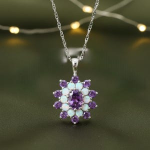 May include: A silver necklace with a pendant featuring a central purple gemstone surrounded by alternating white and purple stones, arranged in a flower-like pattern. The pendant hangs from a delicate silver chain.