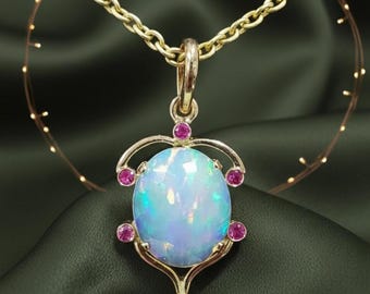 May include: A gold-toned pendant necklace featuring a large, oval opal gemstone with iridescent blue and green hues. The pendant is accented with small, round pink gemstones and hangs from a delicate gold chain. The necklace is displayed on a dark green fabric.