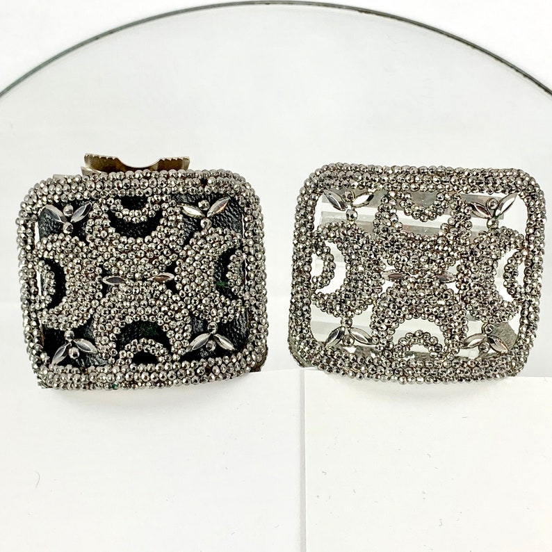May include: Two silver square-shaped brooches with intricate designs made of small beads. The brooches have a geometric pattern with a black background.