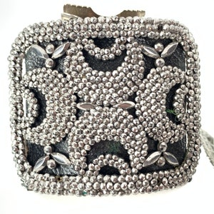 May include: A silver metal box with a decorative pattern of small silver beads. The box has a black background and a geometric design.