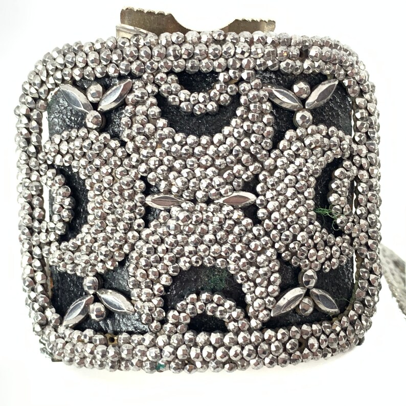 May include: A silver metal box with a decorative pattern of small silver beads. The box has a black background and a geometric design.