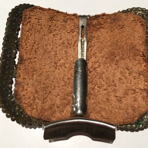May include: A brown leather belt buckle with a silver metal clasp. The buckle is decorated with a chain-like design around the edge.