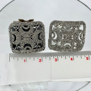 May include: Two silver metal decorative boxes with intricate designs. The boxes are about 2 inches wide and 1.5 inches tall. They are sitting on a white surface with a ruler for scale.