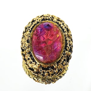 May include: A gold ring with a large, oval-shaped, pink and purple iridescent glass stone set in a detailed, ornate frame.