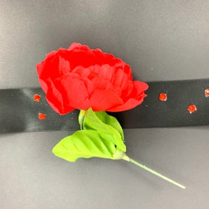 May include: A single red fabric rose with green leaves and a long stem, attached to a black ribbon with red rhinestones.