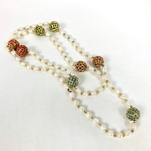 May include: A long white pearl necklace with colorful, gold-toned, jeweled balls. The balls are red, green, and blue.