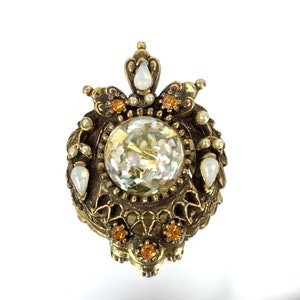 May include: A gold-toned brooch with a large iridescent glass center surrounded by smaller white and orange rhinestones.