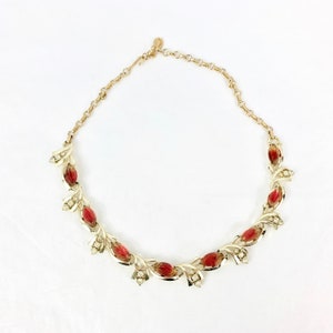 May include: A gold necklace with a delicate chain and red and clear glass stones in a floral design.