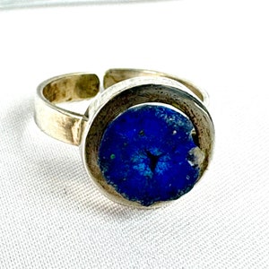 May include: A silver ring featuring a blue stone set in a circular bezel. The stone has a distinctive, textured surface.