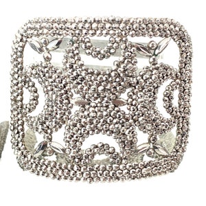 May include: A silver square-shaped bracelet with a delicate, intricate design made of small beads. The bracelet has a geometric pattern with open spaces.
