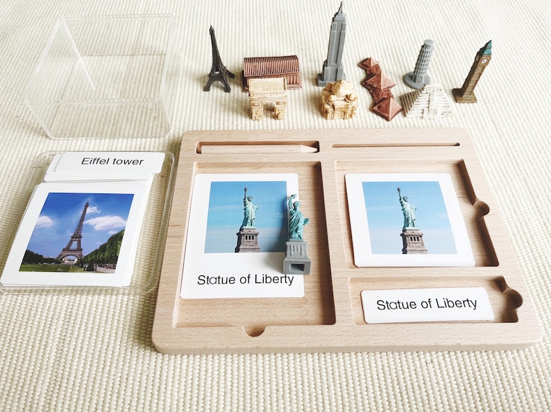 May include: A wooden educational toy set featuring miniature landmarks and matching cards. Includes the Eiffel Tower, Statue of Liberty, and other famous structures. The set includes a wooden tray, cards, and miniature models.