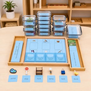 May include: A Montessori-style language learning set featuring clear plastic storage boxes labeled Object Box 1-6 and Picture Box 1-6, a wooden tray with a blue sorting mat, word cards, and miniature objects including a pond, stop sign, rack, lamp, lock, and duck.
