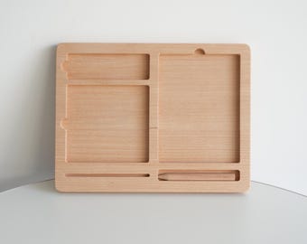 Puede incluir: Un organizador de escritorio de madera clara con múltiples compartimentos. El organizador tiene forma rectangular con varias ranuras y secciones para guardar objetos. La veta de la madera es visible y el diseño es simple y funcional.