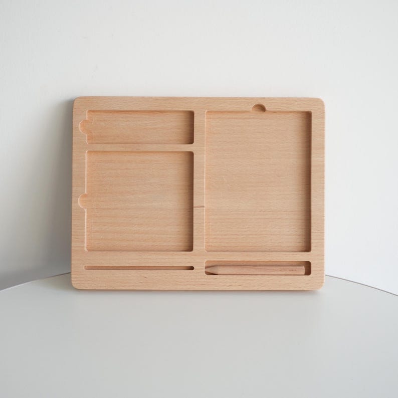 May include: A light-colored wooden desk organizer with multiple compartments. The organizer has a rectangular shape with a variety of slots and sections for storing items. The wood grain is visible, and the design is simple and functional.