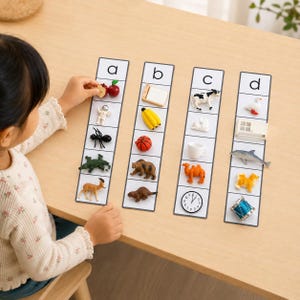 May include: Four vertical white cards labeled a, b, c, and d, each featuring small plastic miniature objects. The cards display items like an apple, astronaut, spider, alligator, deer, bed, banana, basketball, bear, beaver, cow, rabbit, cup, camel, clock, goose, window, dolphin, dog, and drum.