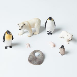 May include: A collection of miniature animal figurines, including polar bears, penguins, and a small nest. The polar bears are white, and the penguins have black, white, and yellow coloring. The nest is a mottled gray color.