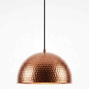 May include: A copper-colored pendant light fixture with a hammered texture dome shade. The light hangs from a black cord and a copper-colored ceiling mount. The fixture is a modern design.