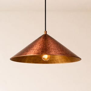 May include: A copper-colored pendant light fixture with a hammered texture. The conical shade has a gold-colored interior and a single light bulb. The fixture hangs from a black cord.