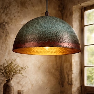 May include: A hanging pendant light with a textured, teal and copper dome shade. The interior of the shade is gold, and a single light bulb is visible. The light fixture hangs from a black cord. The background is a rustic interior.