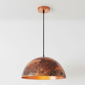 May include: A copper-colored pendant light fixture with a dome-shaped shade. The shade has a textured, aged appearance with brown and orange tones. The fixture hangs from a black cord and a circular ceiling mount.