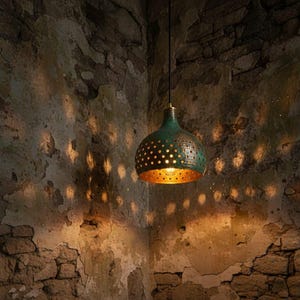 May include: A hanging pendant light with a teal and gold finish. The light fixture has a perforated design, allowing light to shine through. The light is suspended from a black cord in a rustic setting with stone walls.