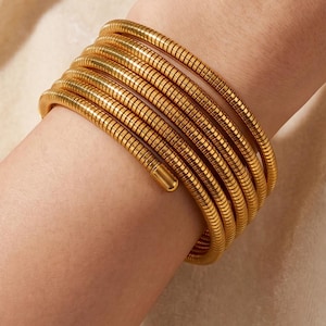 Könnte beinhalten: Ein goldfarbenes Spiralarmband mit einem durchgehenden, flexiblen, schlangenartigen Kettenmuster, das sich mehrfach um das Handgelenk wickelt. Das Armband hat eine glatte, polierte Oberfläche mit einer abgerundeten Endkappe für einen Lagen-Look.
