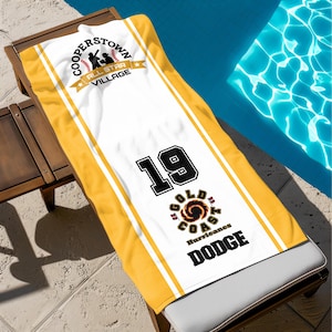 May include: A white and yellow beach towel featuring the text "Cooperstown All Star Village" and "Gold Coast Hurricanes Dodge". The towel has the number 19 in black.