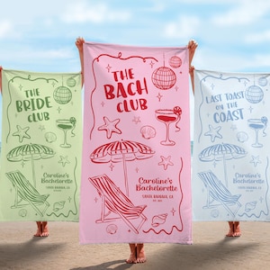 Pode incluir: Tr&ecirc;s toalhas de praia com designs tem&aacute;ticos. Uma &eacute; verde claro com o texto "The Bride Club", outra &eacute; rosa com "The Bach Club", e a terceira &eacute; azul claro com "Last Toast on the Coast". Cada toalha apresenta ilustra&ccedil;&otilde;es com tema de praia.