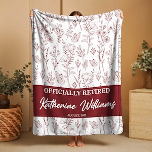 May include: A white blanket featuring a burgundy floral and butterfly design. The blanket has a burgundy band with the text "OFFICIALLY RETIRED" and the name "Katherine Williams" with the date "AUGUST, 2025".