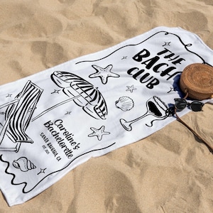 Pode incluir: Toalha de praia branca com ilustra&ccedil;&otilde;es pretas de uma cadeira de praia, guarda-sol, conchas e um copo de cocktail. A toalha diz "The Bach Club" e "Caroline's Bachelorette Santa Barbara, CA EST. 2015". Uma bolsa redonda de tecido e &oacute;culos de sol est&atilde;o na areia.