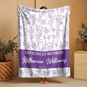 May include: A white blanket featuring a purple floral and butterfly design. The blanket has a purple band with the text "OFFICIALLY RETIRED" and the name "Katherine Williams" with the date "AUGUST, 2025".