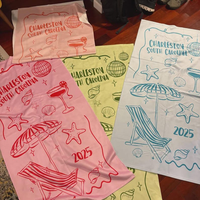 Pode incluir: Toalhas de praia em rosa, amarelo e branco, cada uma com um design de Charleston, Carolina do Sul. As toalhas exibem ilustra&ccedil;&otilde;es de uma bola de discoteca, cocktail, estrelas do mar e uma cadeira de praia. O ano de 2025 est&aacute; impresso em algumas.