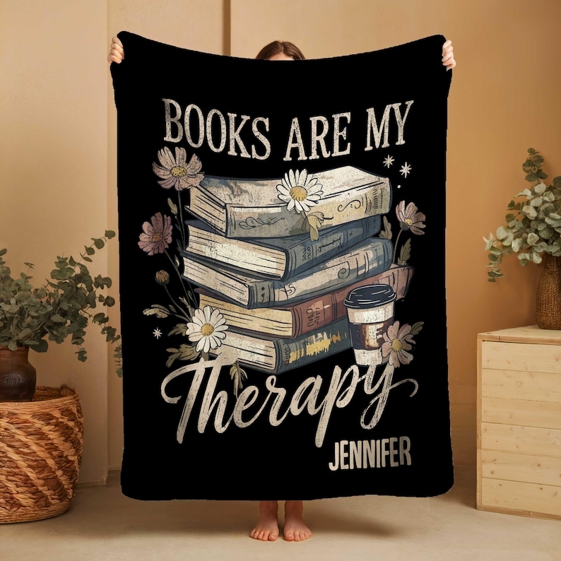 Peut inclure: Couverture noire avec le texte "BOOKS ARE MY Therapy" et le nom "Jennifer". Le motif repr&eacute;sente une pile de livres, des marguerites et une tasse de caf&eacute;. Un article de d&eacute;coration int&eacute;rieure.