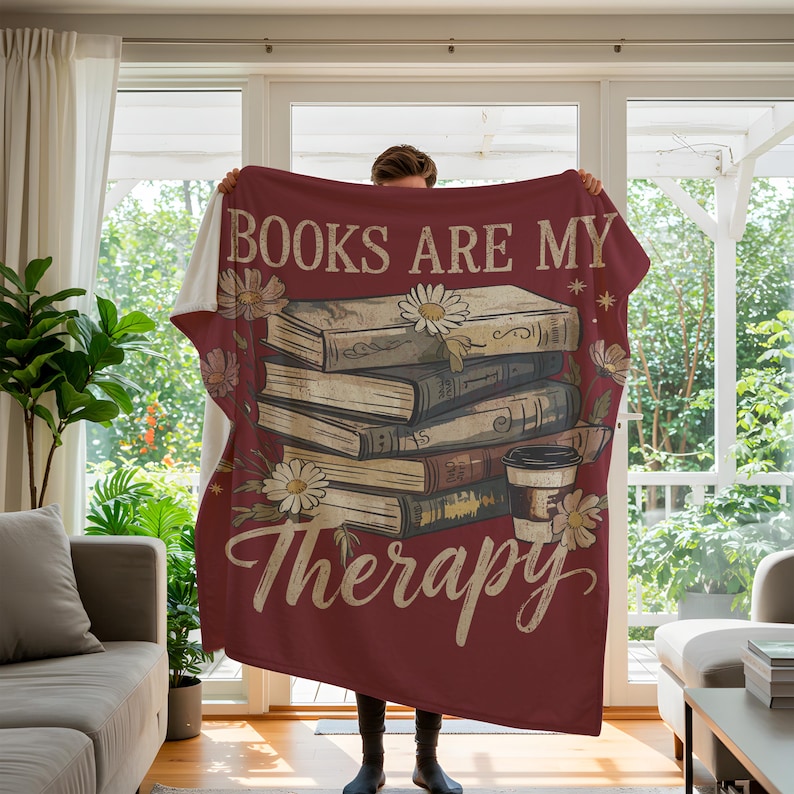 Peut inclure: Une couverture bordeaux avec l'inscription "BOOKS ARE MY Therapy" et un motif de livres, de marguerites et d'une tasse de caf&eacute;. La couverture est pr&eacute;sent&eacute;e, mettant en valeur sa texture douce et son design d&eacute;coratif.