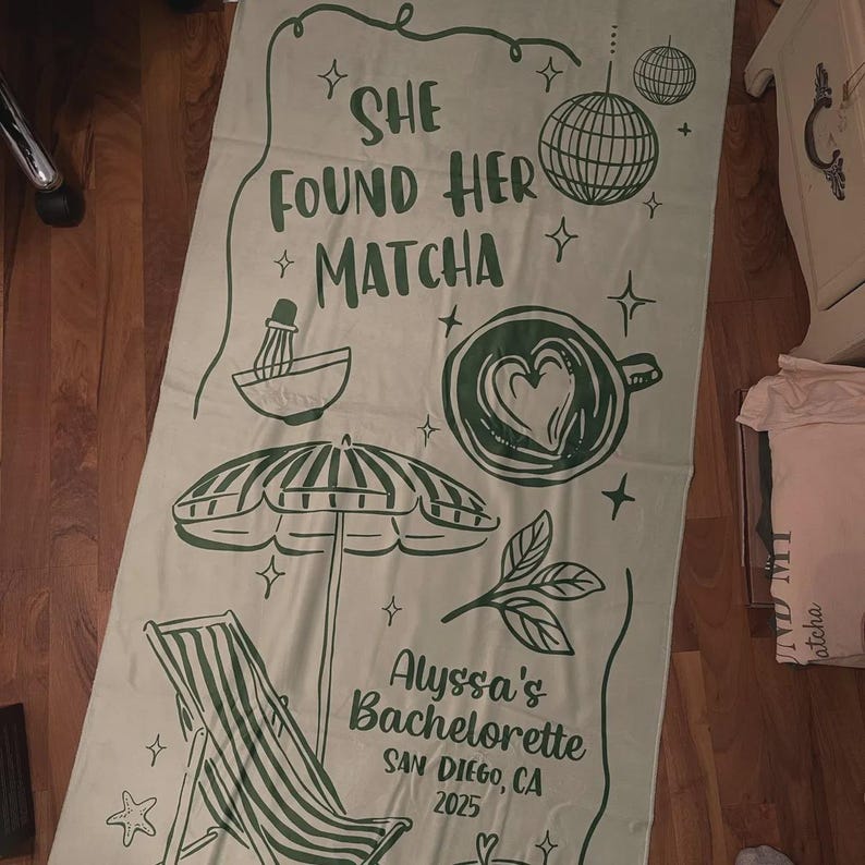Pode incluir: Uma toalha de praia verde claro com tema matcha. A toalha apresenta o texto "SHE FOUND HER *MATCHA" e ilustra&ccedil;&otilde;es de um batedor de matcha, uma x&iacute;cara de caf&eacute; com um cora&ccedil;&atilde;o, um guarda-sol e uma cadeira de praia. O texto "Alyssa's Bachelorette SAN DIEGO, CA 2025" tamb&eacute;m est&aacute; impresso.