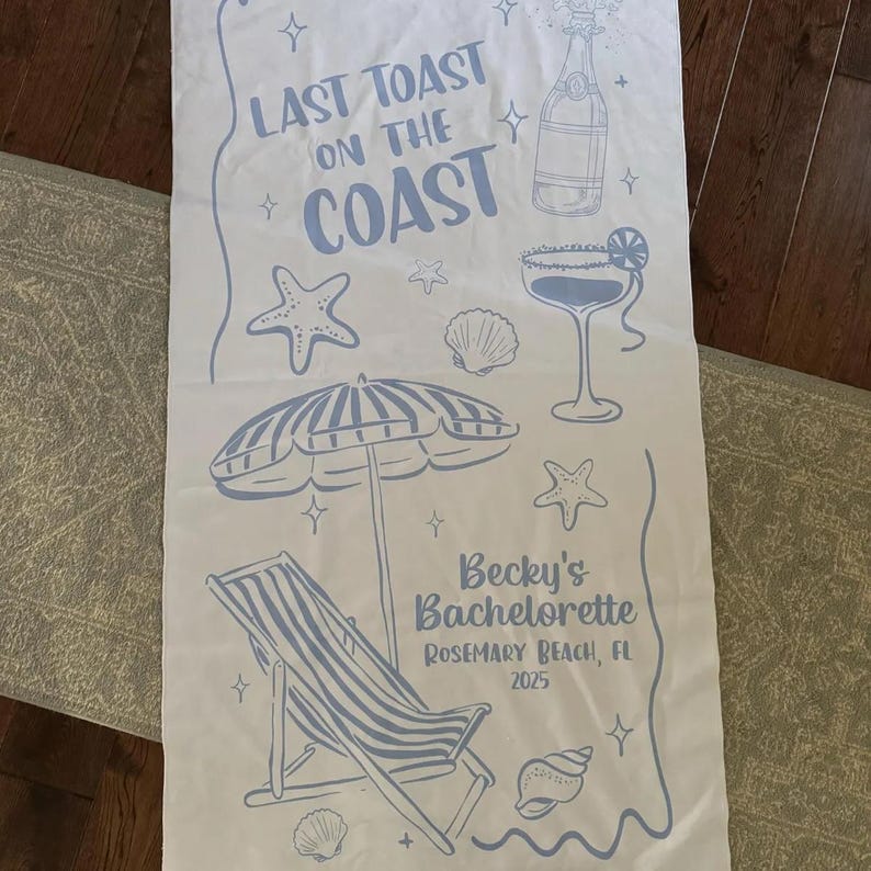 Pode incluir: Toalha de praia branca com ilustra&ccedil;&otilde;es azuis de elementos de praia, incluindo uma garrafa de champanhe, um cocktail, uma estrela do mar, uma concha, um guarda-sol e uma cadeira de praia. O texto diz "Last Toast on the Coast" e "Becky's Bachelorette Rosemary Beach, FL 2025".