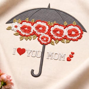 以下が含まれることがあります： 赤と白の花のフラワーアレンジメントが付いた灰色の傘の刺繍デザイン。「I ❤️ YOU MOM」の文字が下に刺繍され、3つの小さな赤いハートが付いています。