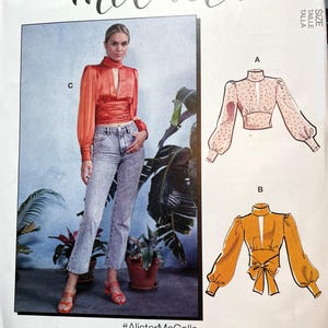 May include: A sewing pattern for a blouse with three different views. The pattern includes a red blouse with a keyhole neckline, a pink blouse with white polka dots, and a yellow blouse with a bow at the waist. The pattern is called #AlisterMcCalls.