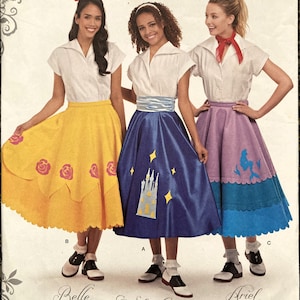 Op de afbeelding: Een naaipatroon voor drie Disney-prinsessenkostuums: Belle, Assepoester en Ariel. Het patroon bevat instructies voor het maken van een wit blouse, een gele rok met rozenversieringen, een blauwe rok met een kasteelontwerp en een gelaagde rok met een zeemeerminontwerp. Het patroon is van Simplicity en is voor maten 6-14.