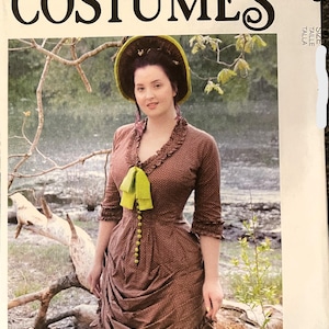May include: A woman in a brown polka-dot dress with a green bow and buttons, and a matching hat. The image is a McCall's Costumes pattern, with the text "COSTUMES" at the top and "Angela Clayton" at the bottom.