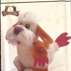 Op de afbeelding: Een Simplicity-knutselpatroon voor het maken van een pluche hond en kip. Het patroon heet "Firffels" en heeft een witte hond met oranje en roze accenten. Het patroonnummer is 7207.