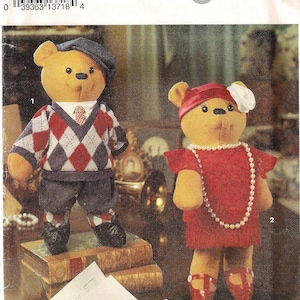 May include: A Simplicity pattern for making two teddy bears. The pattern is for crafts and is number 8265. The bears are dressed in vintage clothing. The male bear is wearing a red and white argyle sweater, blue pants, and a newsboy cap. The female bear is wearing a red dress with a white flower and a string of pearls. The bears are standing on a stack of books.