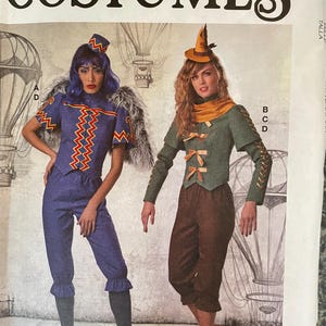 Puede incluir: Patrón de disfraces McCall's con dos diseños. Uno es azul con un diseño en zigzag, el otro es verde y marrón con un sombrero puntiagudo. El fondo incluye globos aerostáticos.