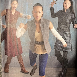 May include: A sewing pattern for three different outfits. The first outfit is a long, burgundy dress with a belt. The second outfit is a brown vest with a tan shirt and blue leggings. The third outfit is a black jacket with a black skirt and leggings. The pattern is from Simplicity and is number 8718.