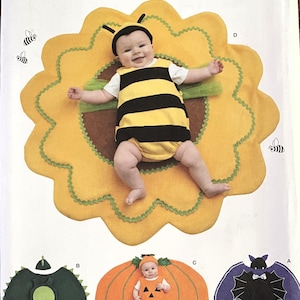 May include: Simplicity Costumes pattern with baby costumes. The image shows a baby dressed as a bee on a yellow flower, and other costume options including a pumpkin, a bat, and a dragon. The pattern is easy-to-sew.