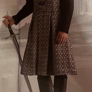 May include: A black and silver patterned tunic with a high collar and long sleeves. The tunic is worn over a black shirt and paired with black boots. A sword is held in the left hand. The text "The Theater Modeste" and "Designed and printed in USA." is visible at the bottom of the image.